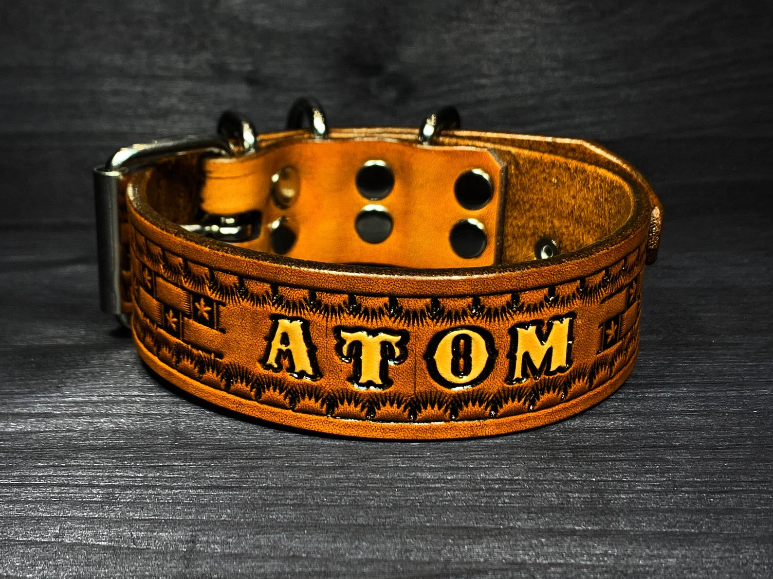 Detail ručně vyráběného koženého obojku pro psa s vyraženým jménem Atom, dekorativní ražba a široké pevné provedení
