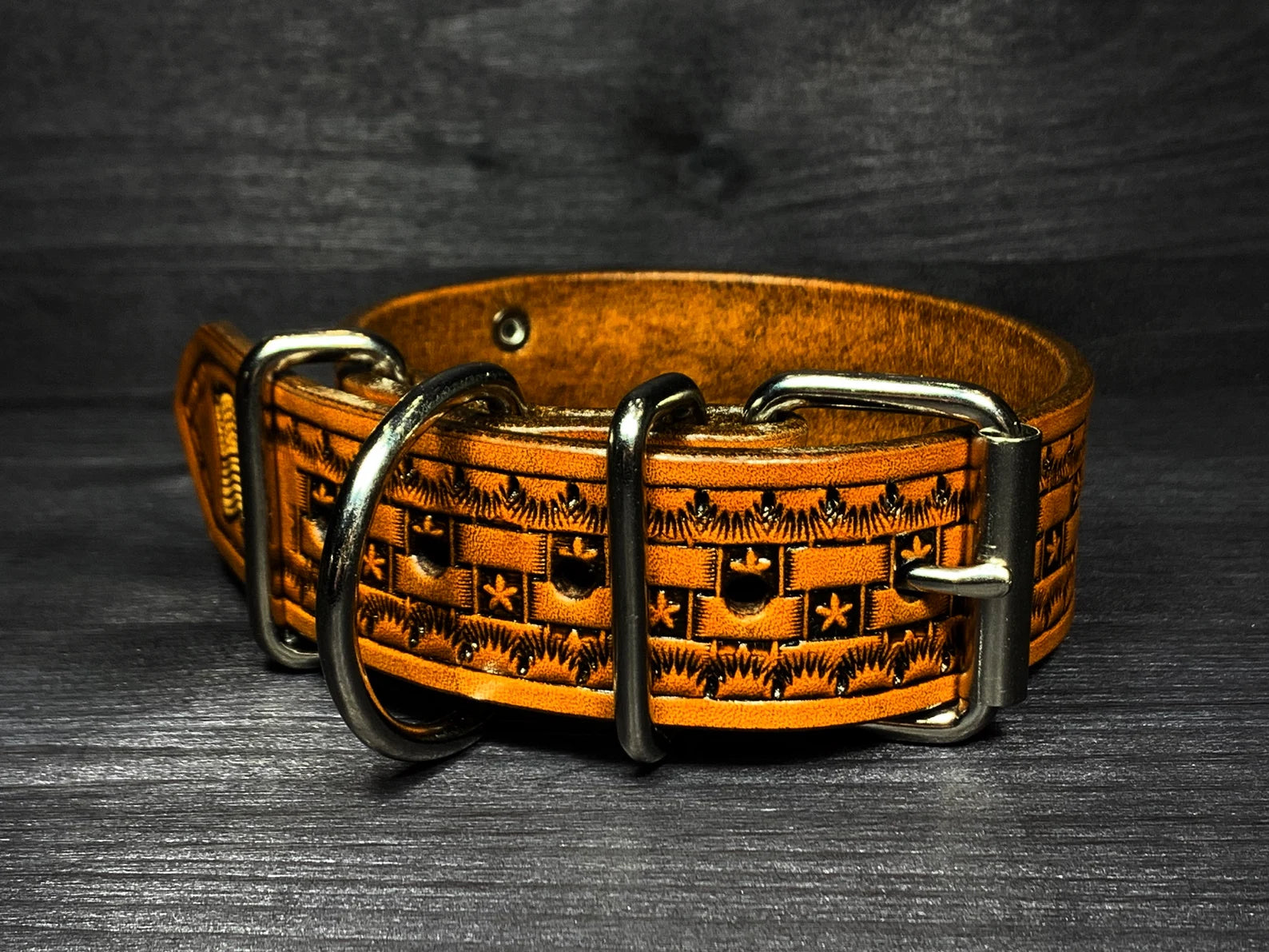 Detail koženého obojku pro psa zepředu s dvojitým kovovým zapínáním, D-kroužkem a ručně raženým vzorem